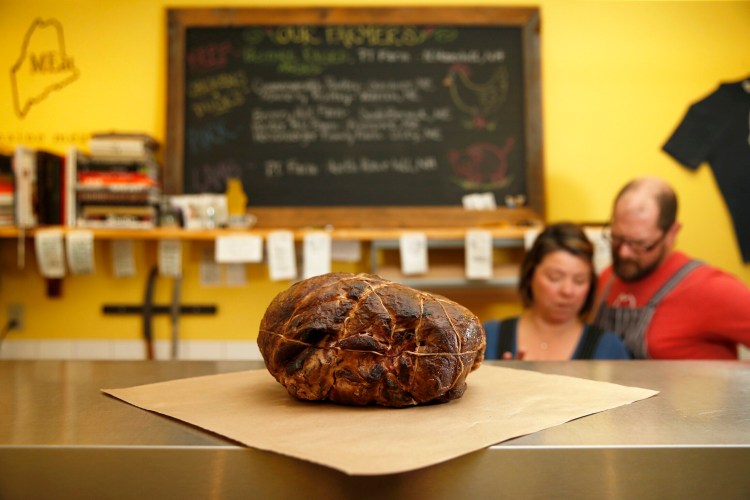 A completed Easter ham rests on the counter at Maine Meat in Kittery while owners Shannon Hill and Jarrod Spangler review orders. 