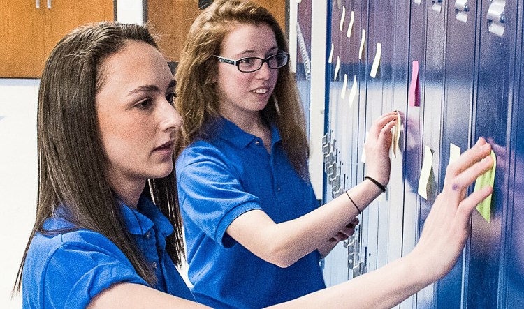 Lewiston Youth Advisory Council members Carolyn Adams, foreground and Emma Williams stick notes to lockers in one of the hallways at Lewiston High School Thursday night.  Students, parents, faculty and community members gathered in the school library to write positive messages with a goal to have one on every locker in the school.