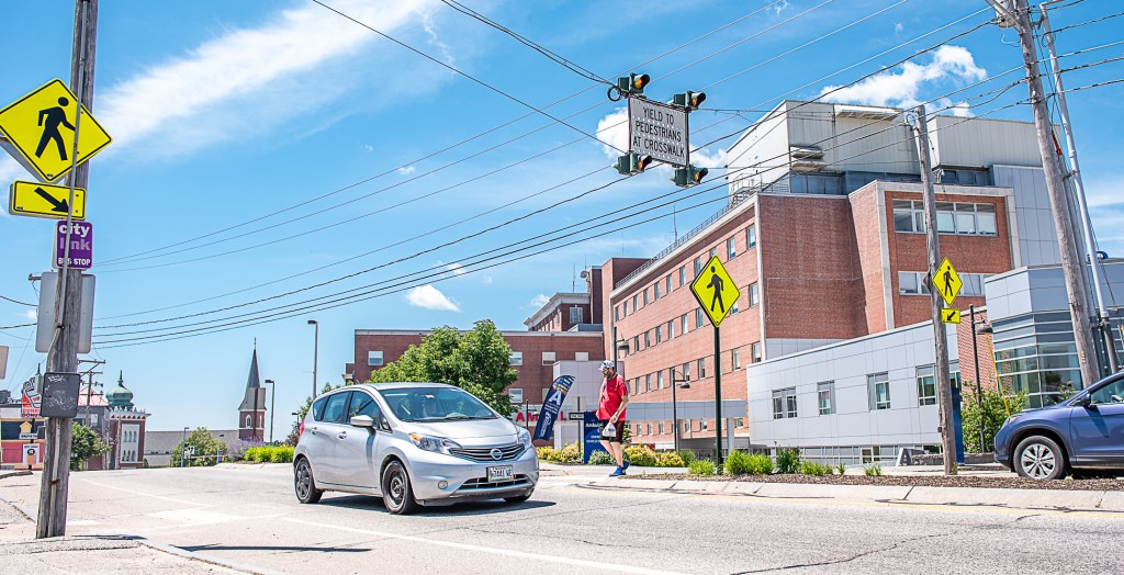 A pedestrian crosses under the broken crosswalk light in front of Central Maine Medical Center on Main Street in Lewiston.