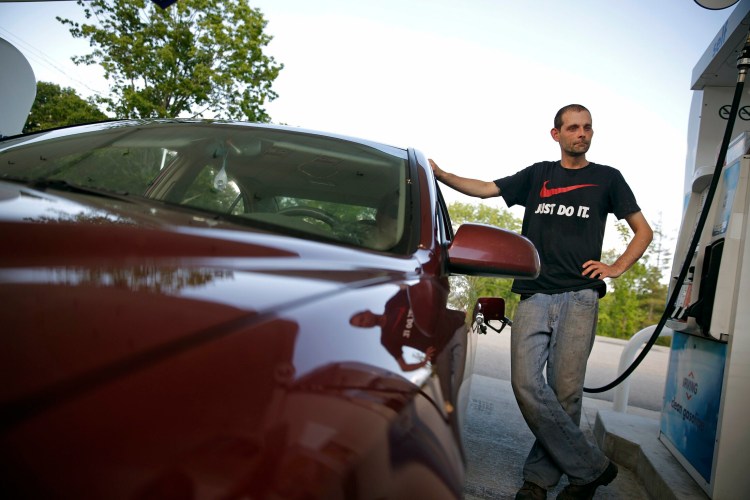 Mike Stafford of Winthrop pumps gas on Congress Street in Portland on Tuesday. Stafford said he texts occasionally while driving to stay in touch with frequent correspondence from his children. A law that takes effect Sept. 19 will make holding a cellphone while driving illegal.