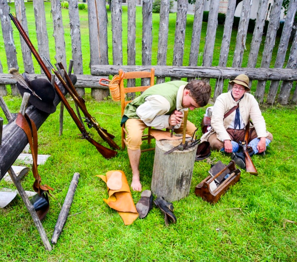 Hannes Moll, left, leans hard on his knife to cut through thick leather while chatting with Rebecca Manthey and making a pair of moccasins Saturday at Old Fort Western in Augusta.