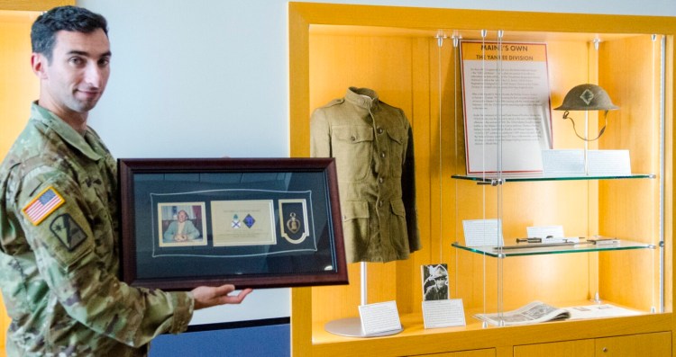 Capt. Jonathan Bratten holds the framed Purple Heart of Sgt. Erroll Wilbert Brawn near where it will be displayed, next to case of World War I items at Camp Chamberlain in Augusta. A presentation was made Thursday by the nonprofit Purple Hearts Reunited.