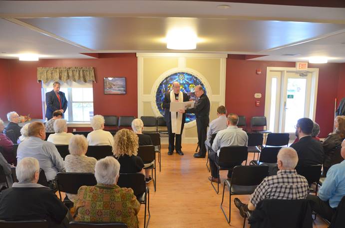 A crowd of residents, family members, and staff sits reverently as Bishop Robert Deeley delivers a prayer of blessing on Wednesday before sprinkling the new addition to St. Francis Apartments, located on 52 Elm St., in Waterville.
