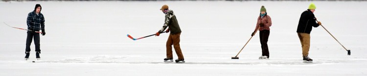 Camden Tweedie, left, passes a puck to Zach Pray as Gia Francis and his brother, Shane Tweedie, brush a fresh coat of snow off Maranacook Lake on Monday in Winthrop. The Winthrop High School students were playing shinny outside on their second week of vacation as the snow commenced.