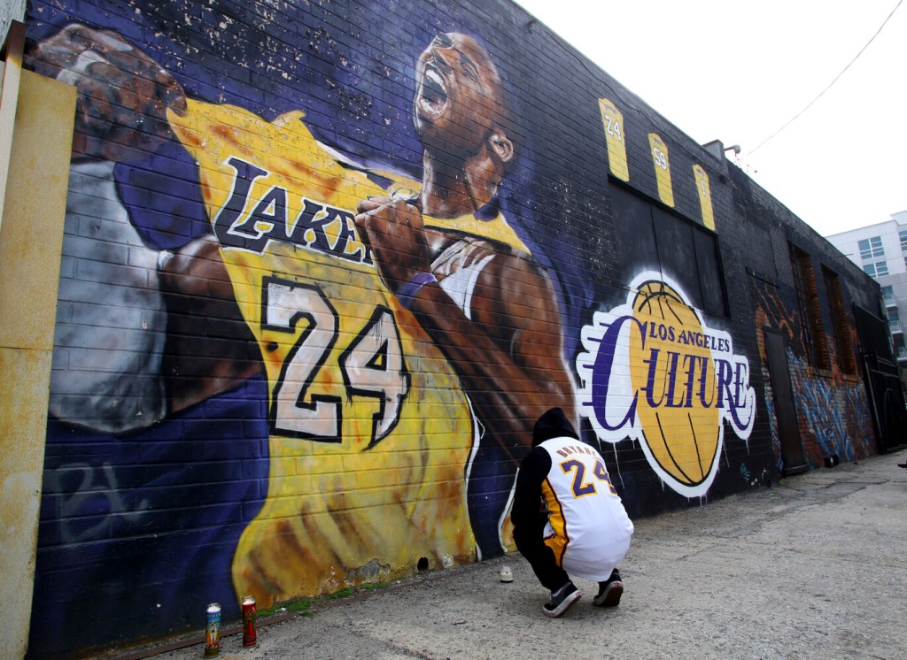 A fan pays respects at a mural depicting Kobe Bryant in a downtown Los Angeles alley after word of the Lakers star's death in a helicopter crash, in downtown Los Angeles Sunday, Jan. 26, 2020. (AP Photo/Matt Hartman)