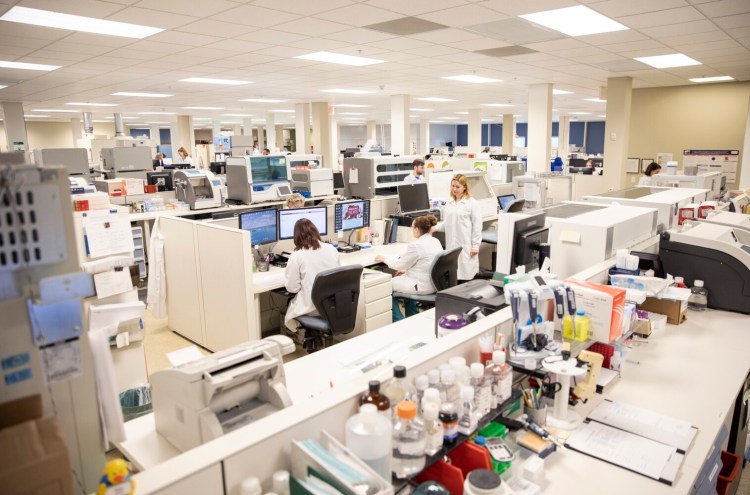 Dr. Hayley Weber, director of molecular biology at NorDx Laboratories, far right, talks with employees  on March 12. NorDx started processing coronavirus tests early in the week and by Thursday they were able to get a result in about 4 hours.