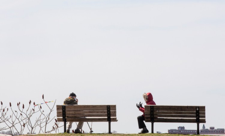 Two people, who declined to give their names, sit six feet apart while taking in the view at Fort Sumner Park on Tuesday. 