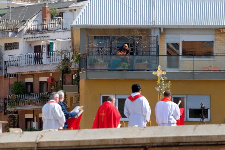 A faithful from a facing balcony follows the celebration of the Palm Sunday Mass on the roof of the church of San Pio X in Rome.
