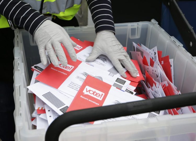 Wearing gloves, a King County Election worker collect ballots from a drop box in the Washington State primary March 10 in Seattle.