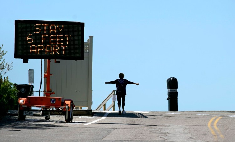 A woman stretches her arms while jogging along Beach Avenue in Kennebunk on Sunday, where a sign is posted advising people to keep six feet apart. 