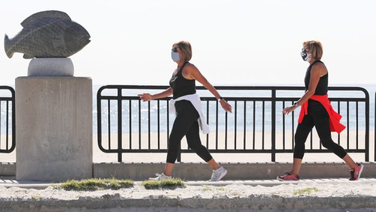 Two women, wearing protective masks due to the COVID-19 virus outbreak, walk on a sidewalk adjacent to an empty Hampton Beach in Hampton, N.H., on Thursday. Beaches in New Hampshire will reopen to swimmers, walkers and runners June 1, but sunbathers will have to wait. 