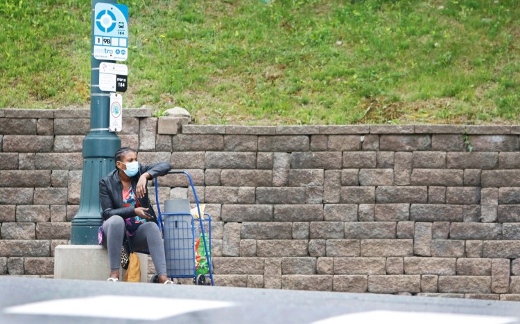 A woman wearing a mask waits for a bus on Congress Street Sunday morning.