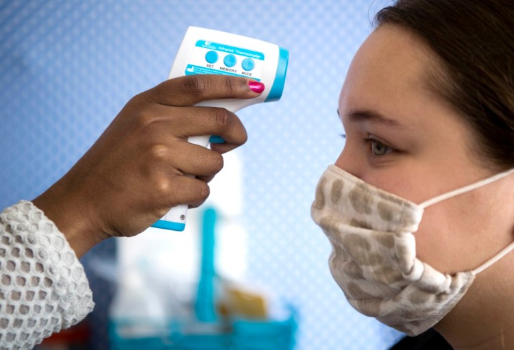 Zainab Salih checks the temperature of coworker Sofia Herron-Donisvitch at the Alfond Youth Center in Waterville on Saturday. Everyone entering the facility will have their temperature taken under the new guidelines.