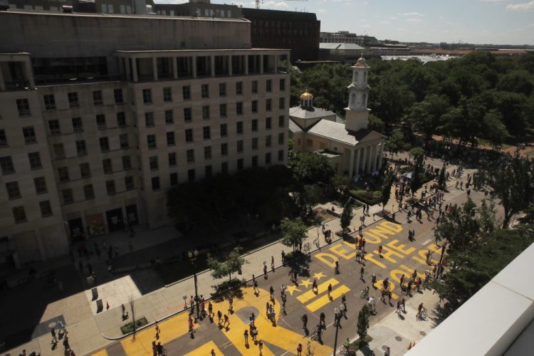 People walk on the words "defund the police" that was painted in bright yellow letters on 16th Street as demonstrators protest Sunday near the White House. 