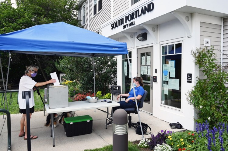 Holly Haywood drops her absentee ballot into a ballot box outside South Portland City Hall on Monday as city worker Jenee Pelletier watches.