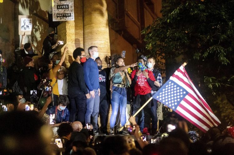 Black Lives Matter organizer Teal Lindseth, 21, addresses protesters as Portland Mayor Ted Wheeler, left, listens on Wednesday in Portland, Ore. Late Wednesday Wheeler joined protesters at the front of the crowd and was hit with chemical irritants several times by federal officers dispersing demons

 