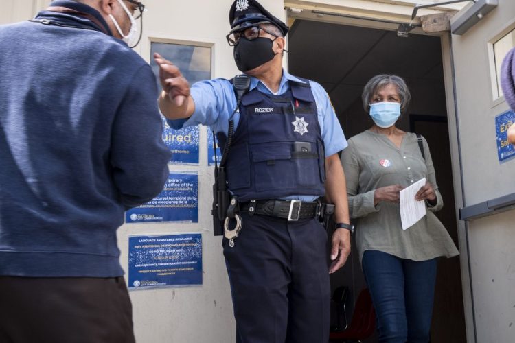 A Philadelphia Sheriffs Deputy clears the door for a voter to exit at a satellite election office at Overbrook High School on Thursday in Philadelphia. The city of Philadelphia has opened several satellite election offices and more are slated to open in the coming weeks where voters can drop off their mail in ballots before Election Day.