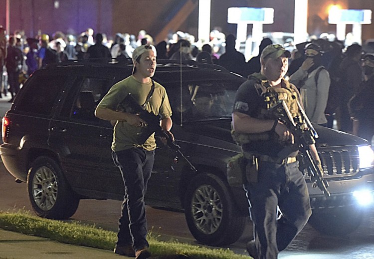 Kyle Rittenhouse, left, with backwards cap, walks along Sheridan Road in Kenosha, Wis., with another armed civilian on Aug. 25. Rittenhouse was among a number of armed white men who converged on the city this summer, claiming to protect property owners from arson and theft, one example of political or social unrest that has caused increased anxiety levels among Blacks. 