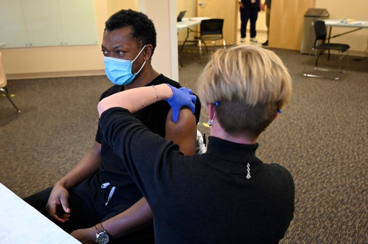 Dr. Jules Bodo is prepped to receive a COVID-19 vaccination at Rumford Hospital, part of the Central Maine Healthcare network, by Bobbie Olsen, a registered nurse, in December. As of Monday, 12.98 percent of Maine’s 1.3 million people had received their first dose.