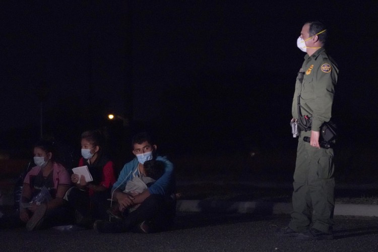 A migrant man holds a child as he looks at a U.S. Customs and Border Protection agent at an intake area after crossing the U.S.-Mexico border, early Wednesday in Roma, Texas. A surge of migrants on the Southwest border has the Biden administration on the defensive. 