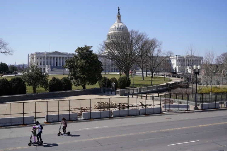 People ride scooters past an inner perimeter of security fencing on Capitol Hill in Washington, Sunday, March 21.