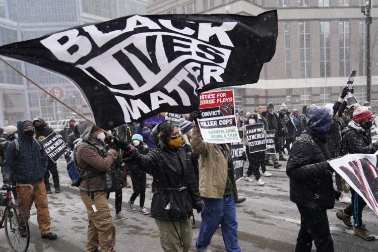 A group of protesters march in the snow around the Hennepin County Government Center on Monday in Minneapolis, where the second week of jury selection continues in the trial for former Minneapolis police officer Derek Chauvin. 