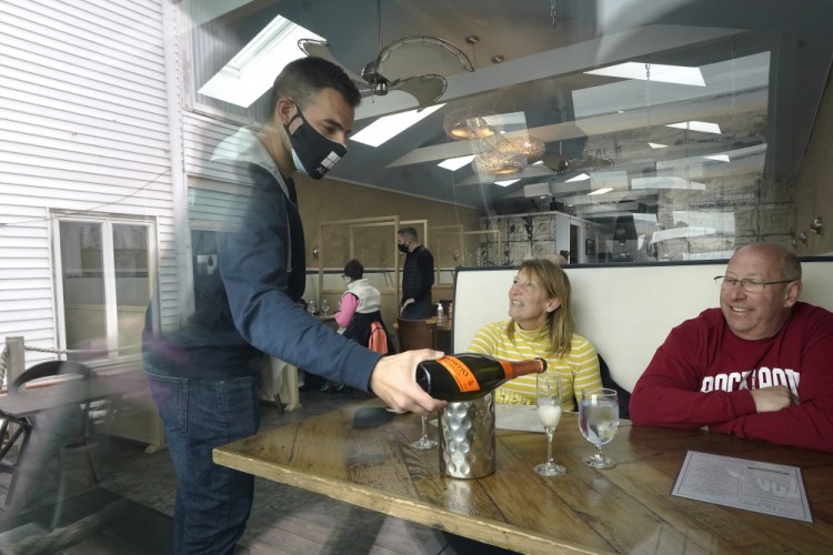 Bartender Denis Angelov, of Provincetown, Mass., serves Julie Skaller and her husband, David Skaller, both of Brewster, N.Y., at Tin Pan Alley restaurant  in Provincetown in April. Data from a later coronavirus outbreak in Provincetown provided key information that prompted the U.S. CDC this week to recommend that even vaccinated people wear masks in some indoor public settings.