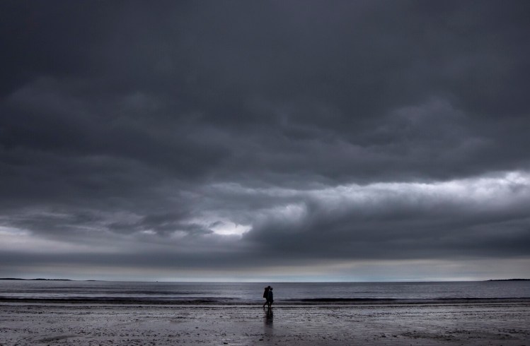 A couple walk along the sand at Old Orchard Beach on Monday afternoon under ominous skies. The rainy weather this month has helped ease drought conditions in parts of Maine, even if it isn't exactly what tourist businesses might have preferred.