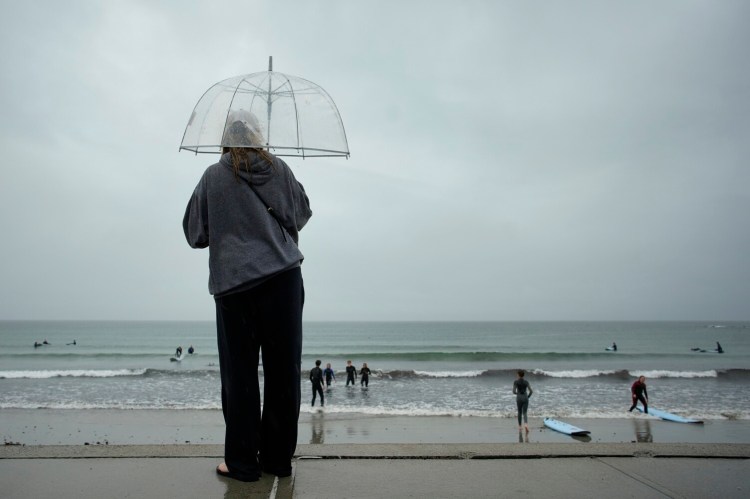 Jenny Shanley holds an umbrella to shield herself from a driving rain while watching a surfing class at Gooch’s Beach in Kennebunk on Friday. Despite the rain, drought conditions persist in Maine. 