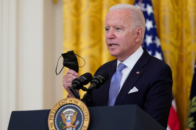 President Biden holds a face mask as he announces that millions of federal workers must show proof they've received a coronavirus vaccine or submit to regular testing and stringent social distancing, masking and travel restrictions in an order to combat the spread of the coronavirus, on Thursday at the White House in Washington, D.C. 