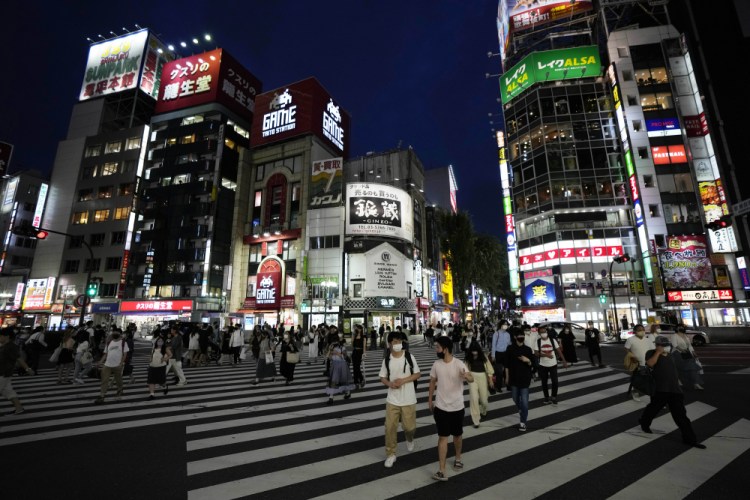 People walk along a pedestrian crossing Friday, July 30, 2021, in Tokyo, as Japanese Prime Minister Yoshihide Suga expanded a coronavirus state of emergency to four more areas in addition to Tokyo following record spikes in infections as the capital hosts the Olympics.