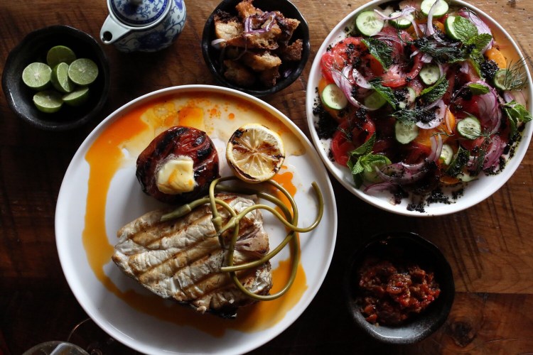 PORTLAND, ME - AUGUST 18: It's tomato season and Jing Yan chef Bijan Eslami prepared several dishes to celebrate the fruit. At bottom right is a Chinese-style romesco sauce made from fire-roasted beefsteak tomatoes, red peppers, garlic and thyme, which is often served with oysters. A fire-roasted, butter-topped beefsteak tomato shares the plate with a halibut steak, cartelized lemon, pickled garlic scapes and chili oil. Heirloom tomatoes are the main attraction in shepherd's tomato salad that includes Persian cucumbers, red onion, dill, mint and topped with lemon-mint vinaigrette. Jing Yan chef Bijan Eslami, who is originally from Iran, said the salad is just like his grandmother used to make. (Staff photo by Ben McCanna/Staff Photographer)