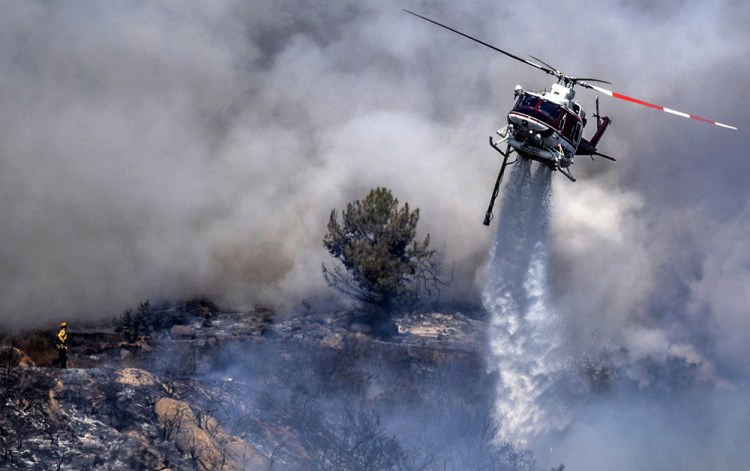 A firefighter is dwarfed by an aerial drop at the the Chaparral Fire in Murrieta, which still blazes Sunday.  Several homes appear to be evacuated in the area. 