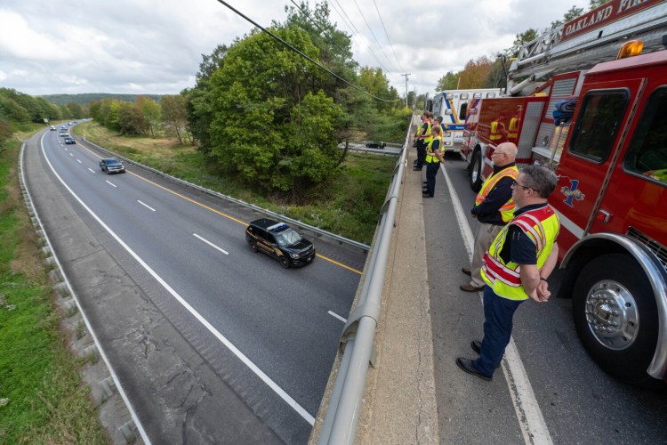 Shon Dixon, front right, and Tim Beales, back right, of Delta Ambulance, stand Thursday on Armstrong Road in Waterville, above Interstate 95, as a police procession carrying the body of Hancock County Sheriff's Deputy Luke Gross heads to the State Medical Examiner's Office in Augusta. Gross was killed early Thursday while responding to a call in Trenton.