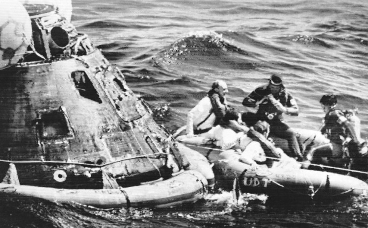 Apollo 16 astronauts, from left wearing white suits, Thomas Kenneth Mattingly, John Young and Charles Duke, pose for photographs by Navy Frogmen in a rubber raft after leaving their spaceship, left, in the Pacific Ocean on April 27, 1972. Associated Press file